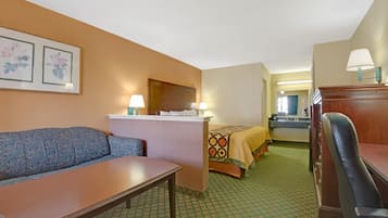 A hotel room with a sofa, a desk, a bed with a patterned bedspread, and a mirror above the bed.