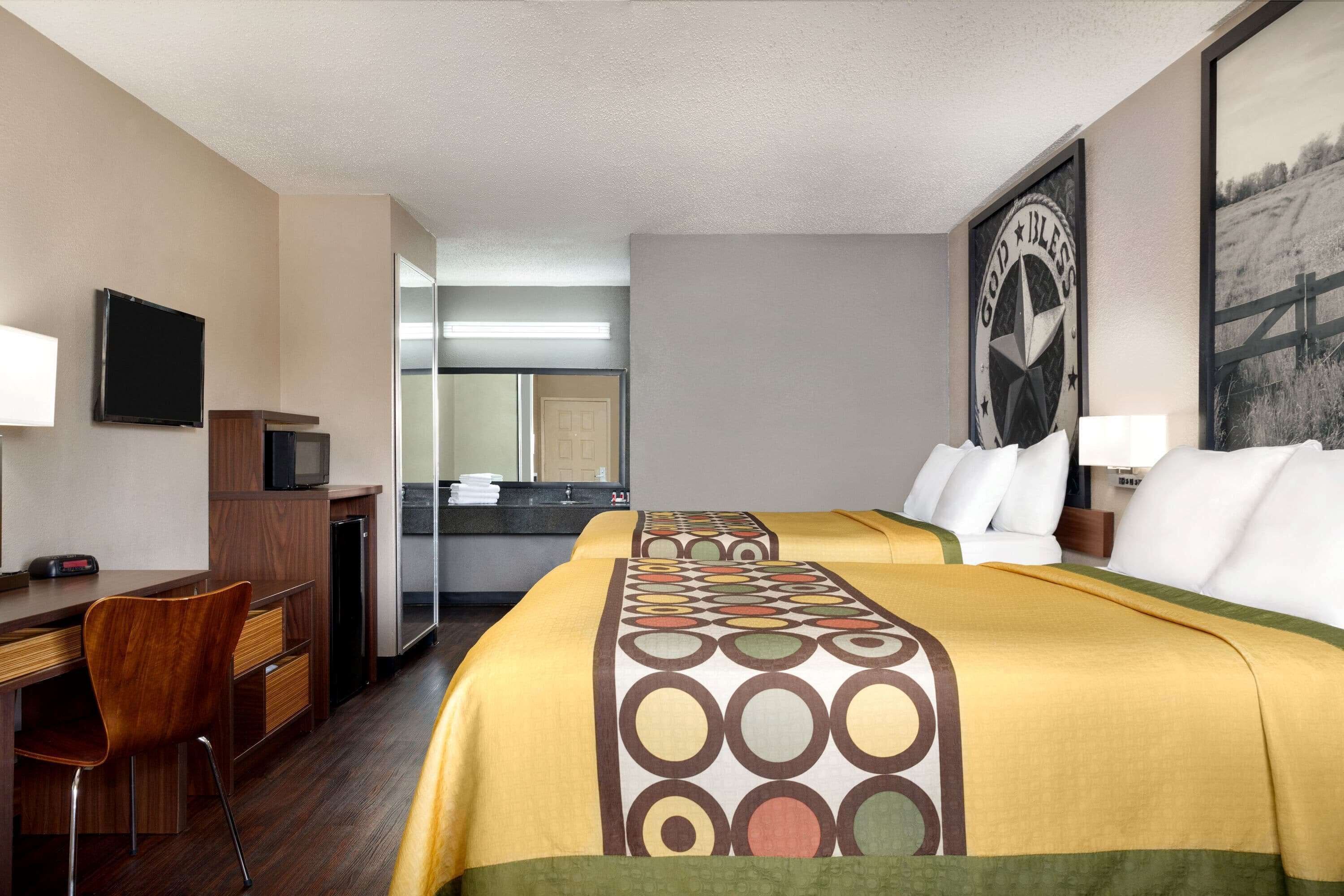 Une chambre d’hôtel avec deux lits, un bureau, une chaise, une télévision et une salle de bain visible à travers une porte ouverte.