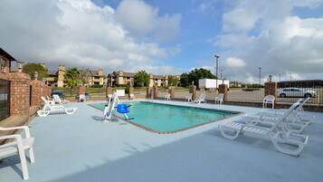A swimming pool with lounge chairs and a blue chair, surrounded by brick walls and a clear sky.