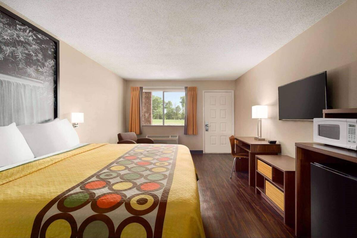 A hotel room with a bed, desk, chair, TV, and a window with curtains.