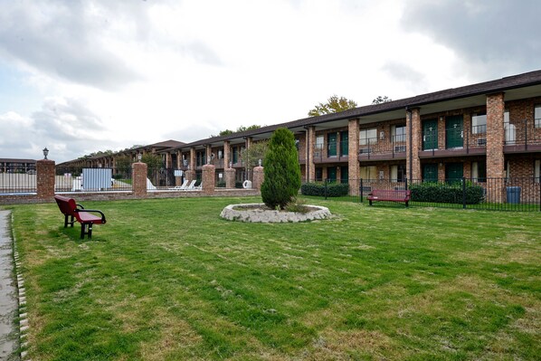 A motel with a grassy courtyard, a central circular planter, and a row of rooms with brick facades and balconies.