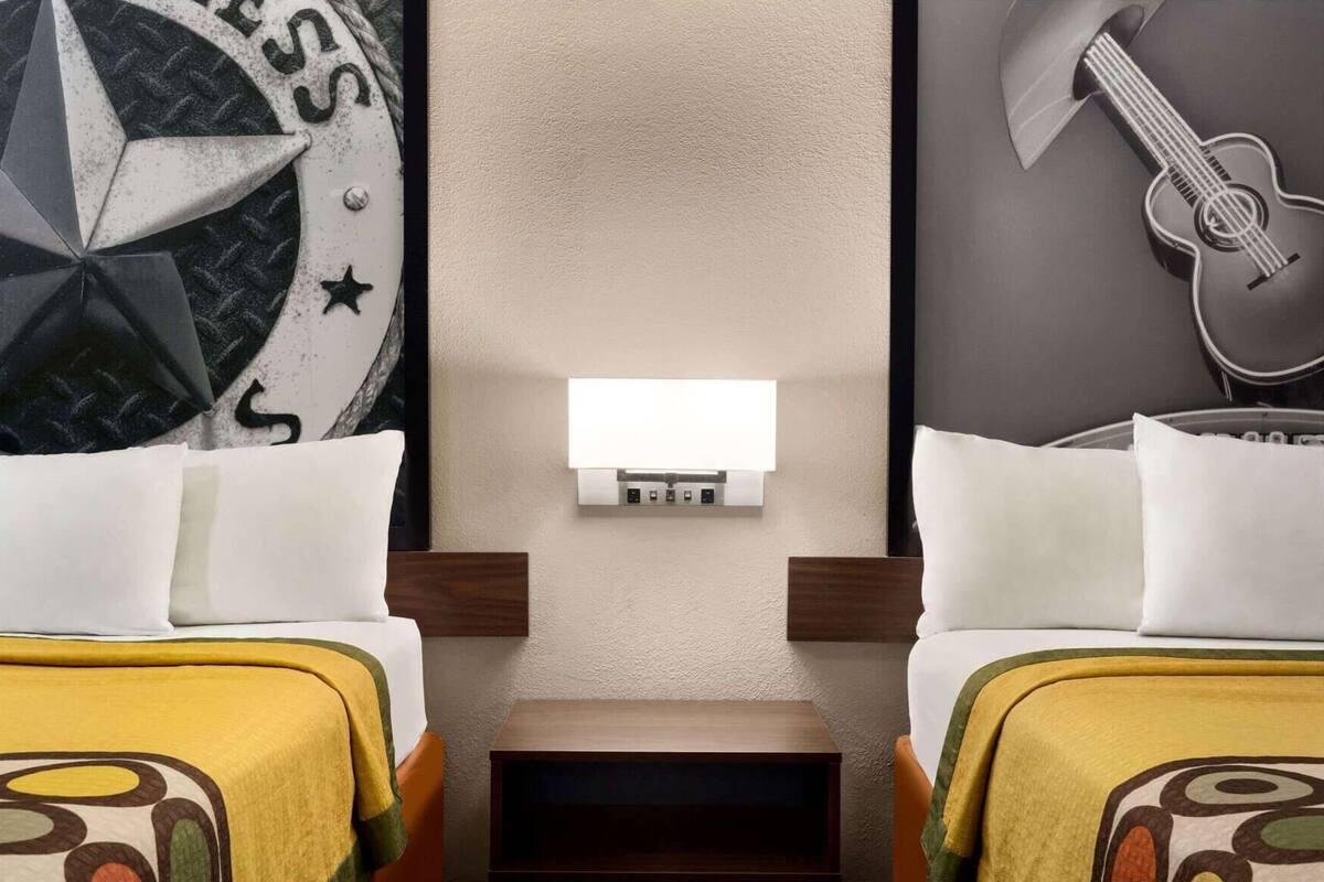 A hotel room with two beds, a wall-mounted light, and a guitar decoration.