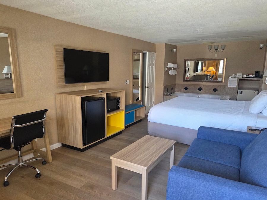 A hotel room with a bed, a TV, a desk, a chair, a small table, and a sofa.