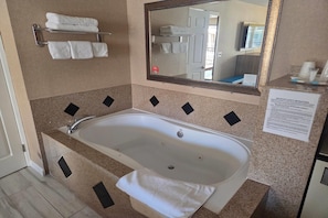 A bathroom with a bathtub, a towel rack with folded towels, a mirror, and a safety instructions sign. - Days Inn by Wyndham Alhambra CA (Alhambra)