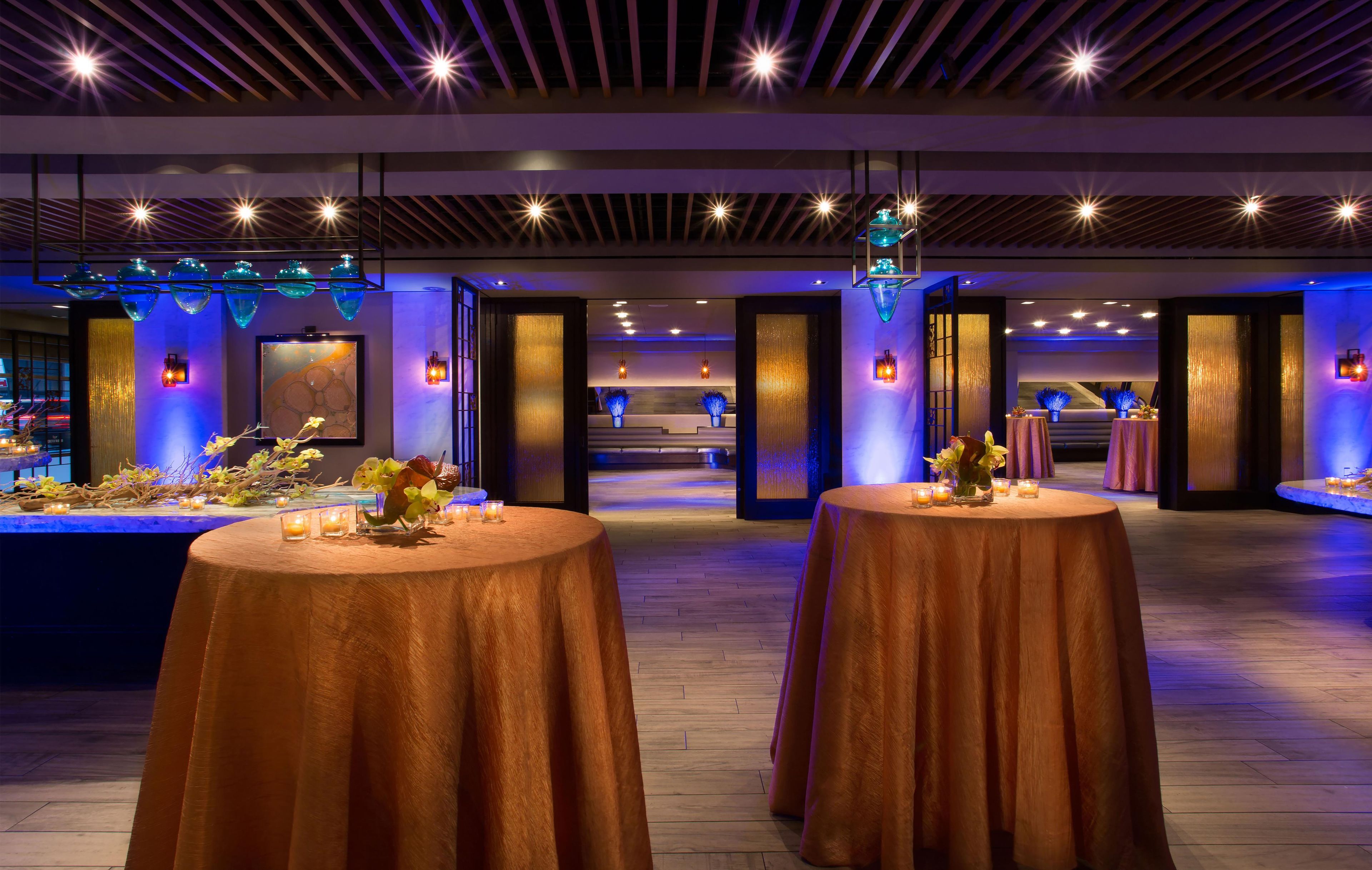A spacious indoor area with multiple round tables, some with candles and flowers, and a reception desk in the background.