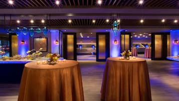 A spacious indoor area with multiple round tables, some with candles and flowers, and a reception desk in the background.