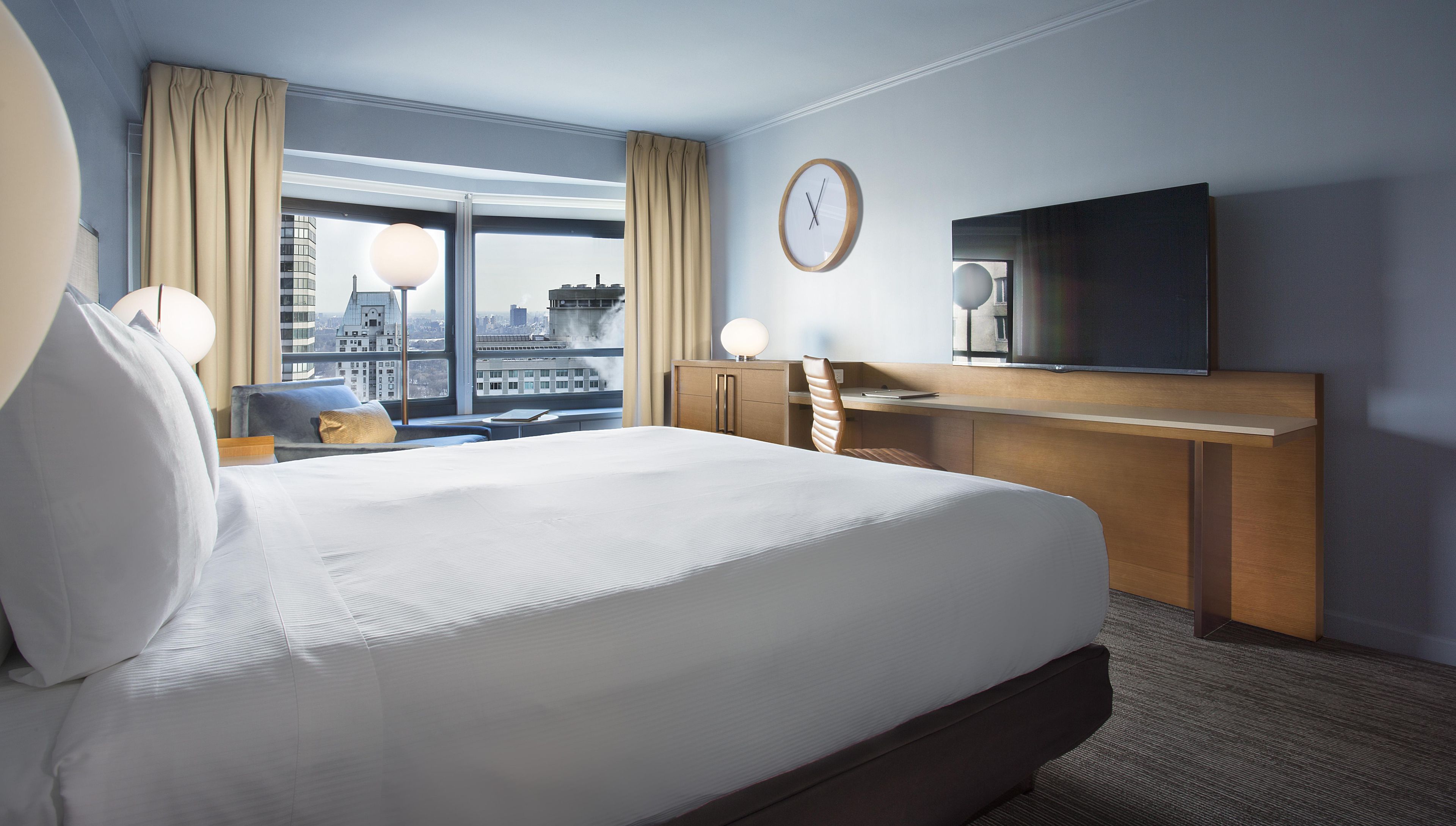 A hotel room with a large bed, a desk, a television, and a view of the city.