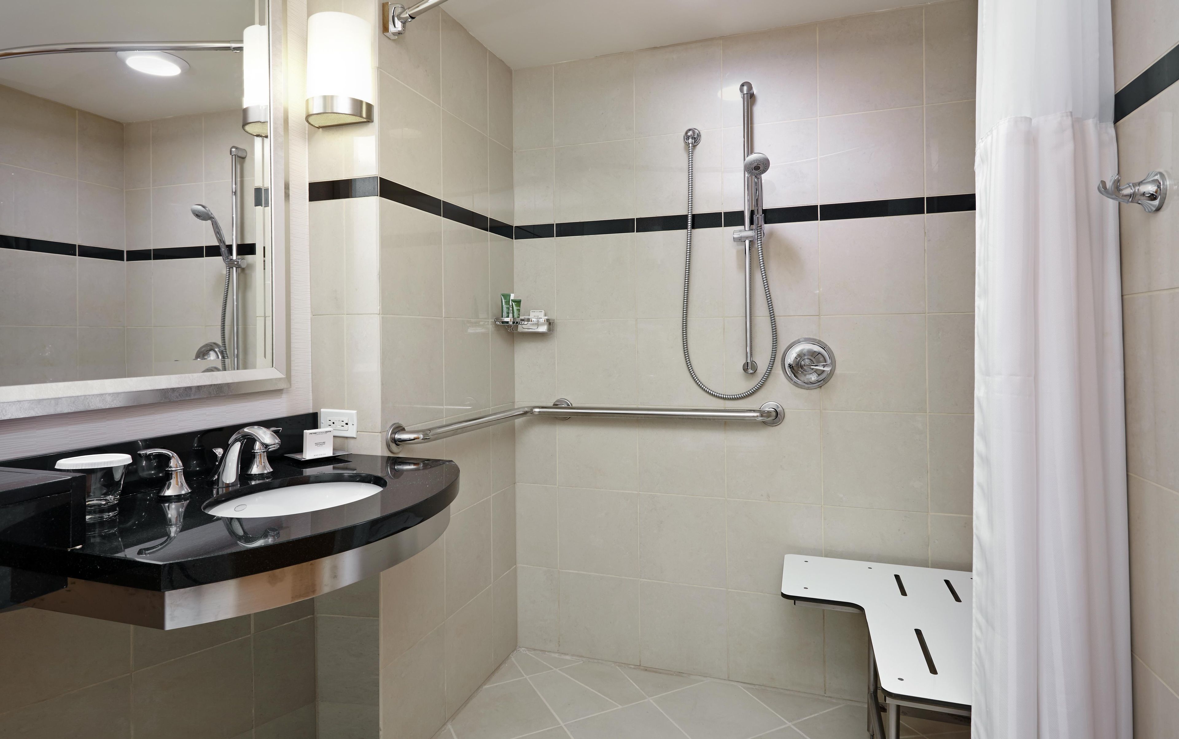 Une salle de bain moderne dotée d’un meuble-lavabo à deux vasques, d’une douchette à main, d’une douche à main et d’une barre d’appui.