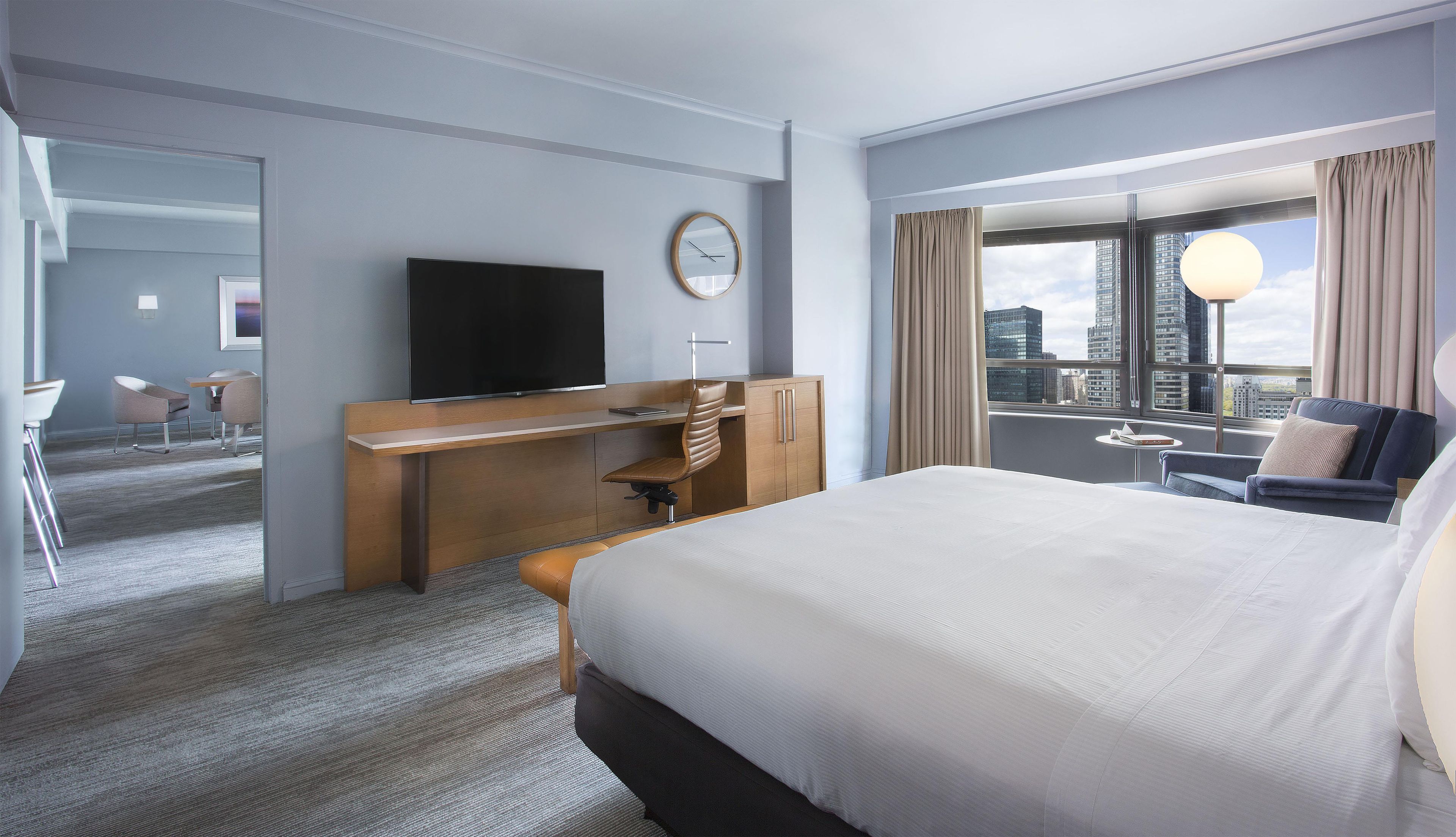 Quarto de hotel com cama, escrivaninha e cadeira, televisão e vista para a cidade.