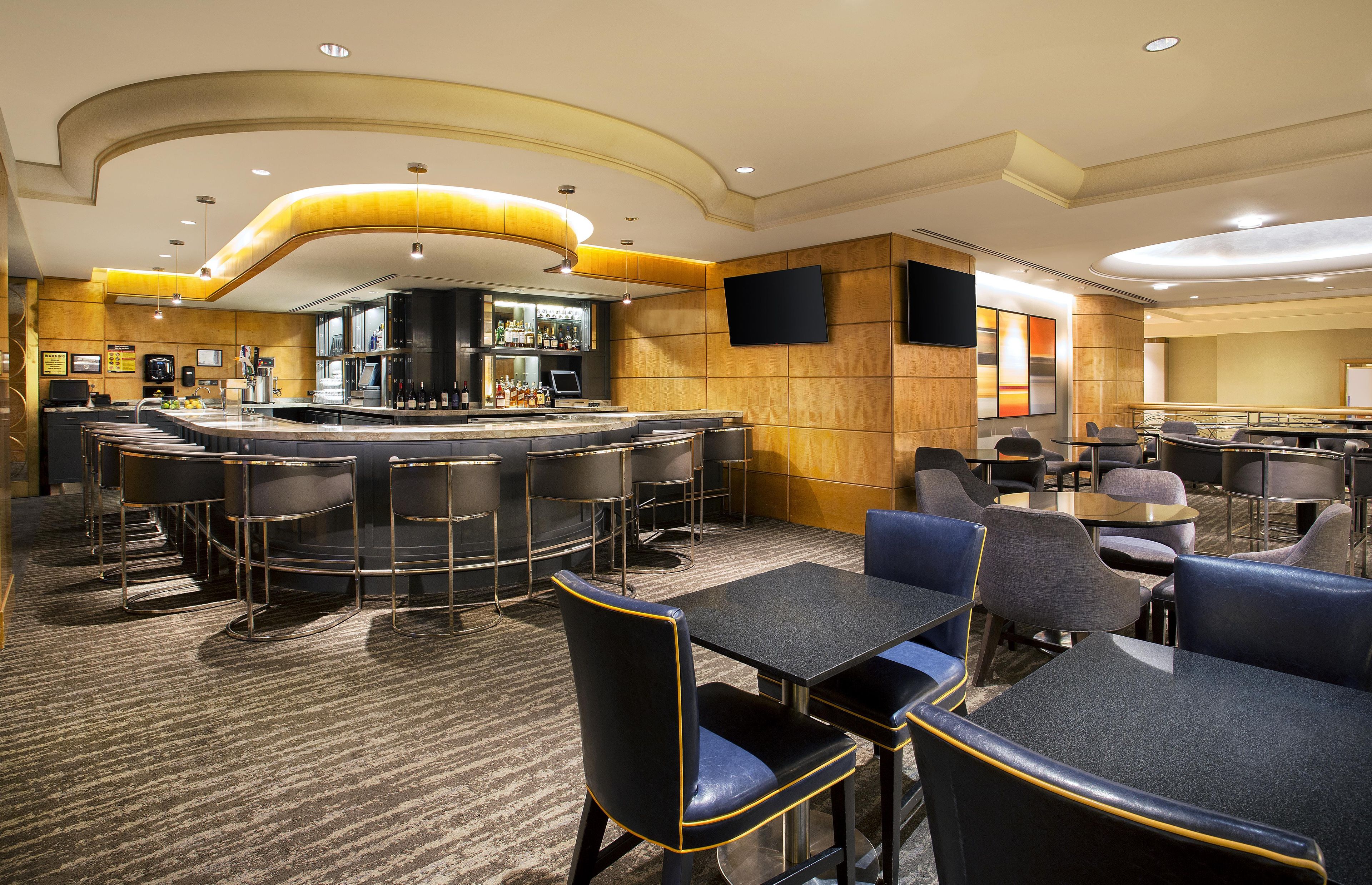 A hotel lobby with a bar area, seating arrangements, and a television screen.