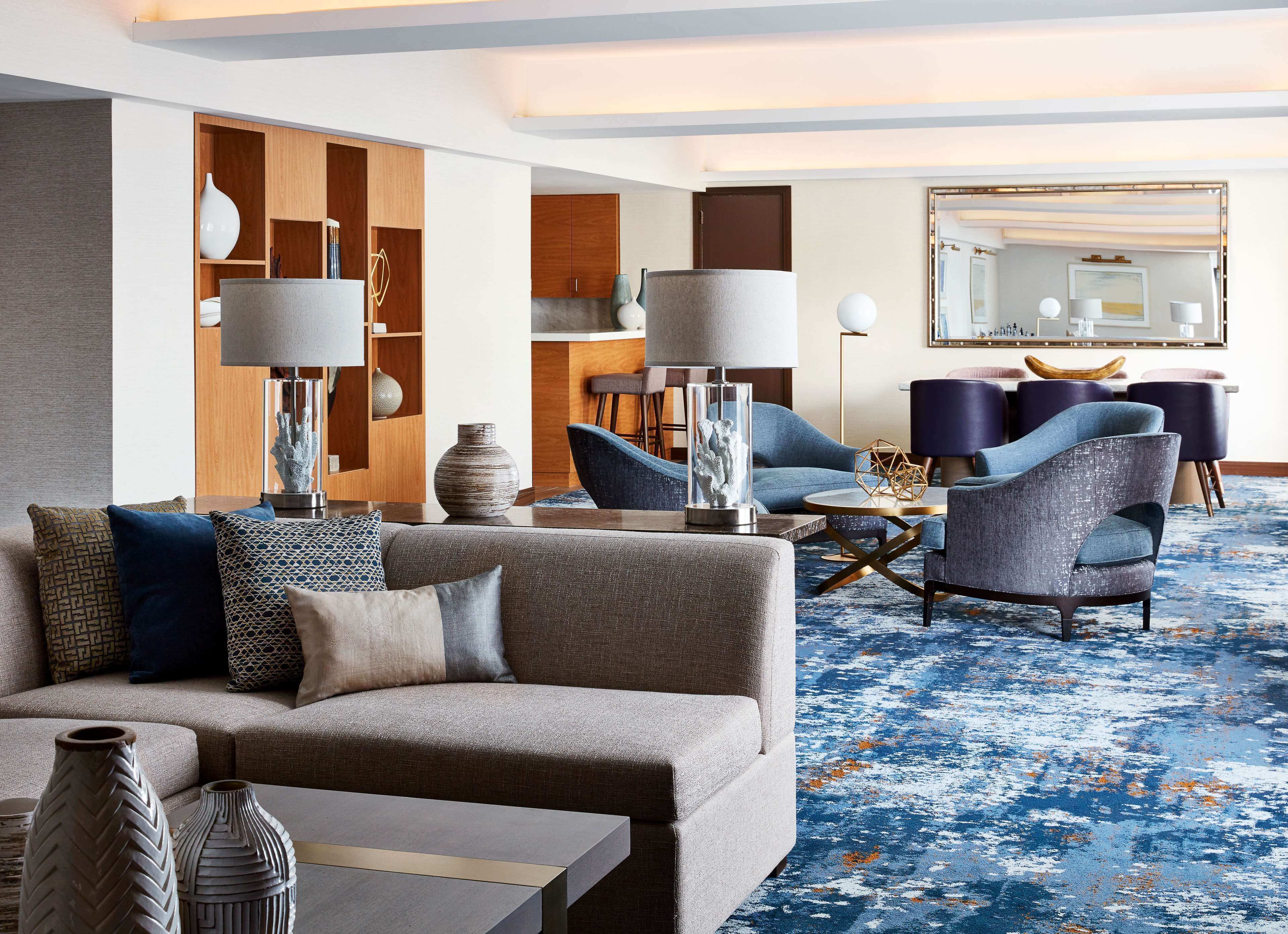 Un hall d’hôtel moderne avec un canapé gris, des fauteuils bleus et un tapis à motifs.