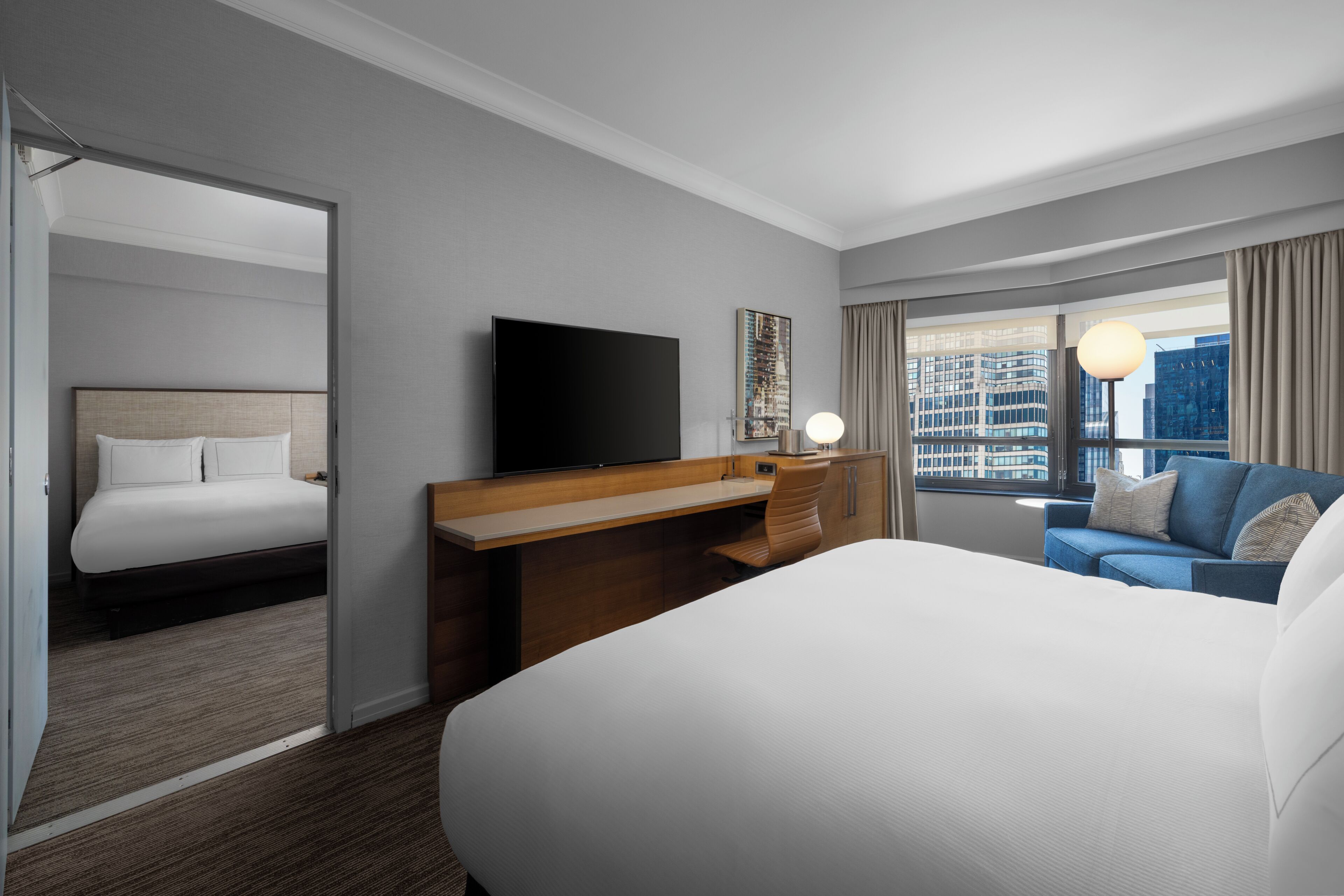 Habitación de hotel con una cama grande, un escritorio, televisión y vistas a la ciudad.