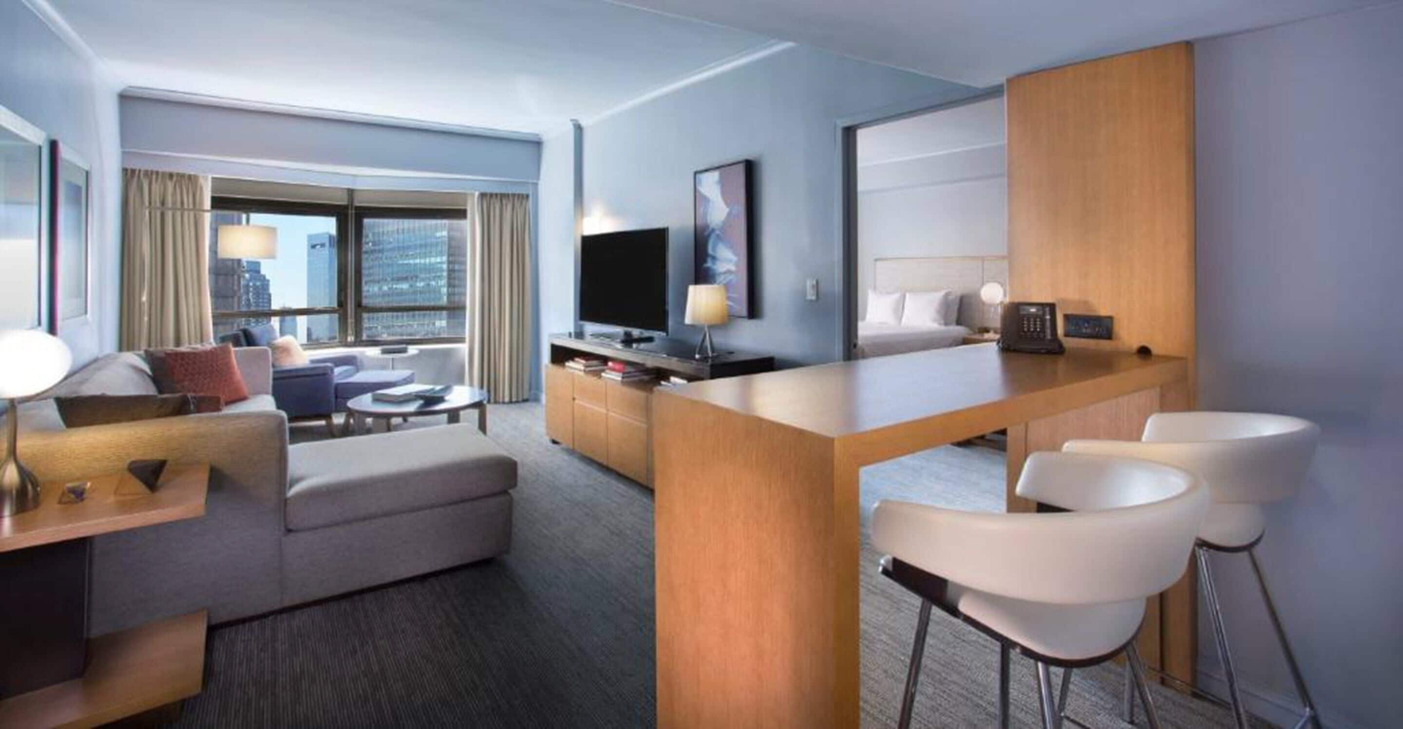 Een moderne hotelkamer met een bank, een eettafeltje, een televisie en een bureau met twee stoelen.
