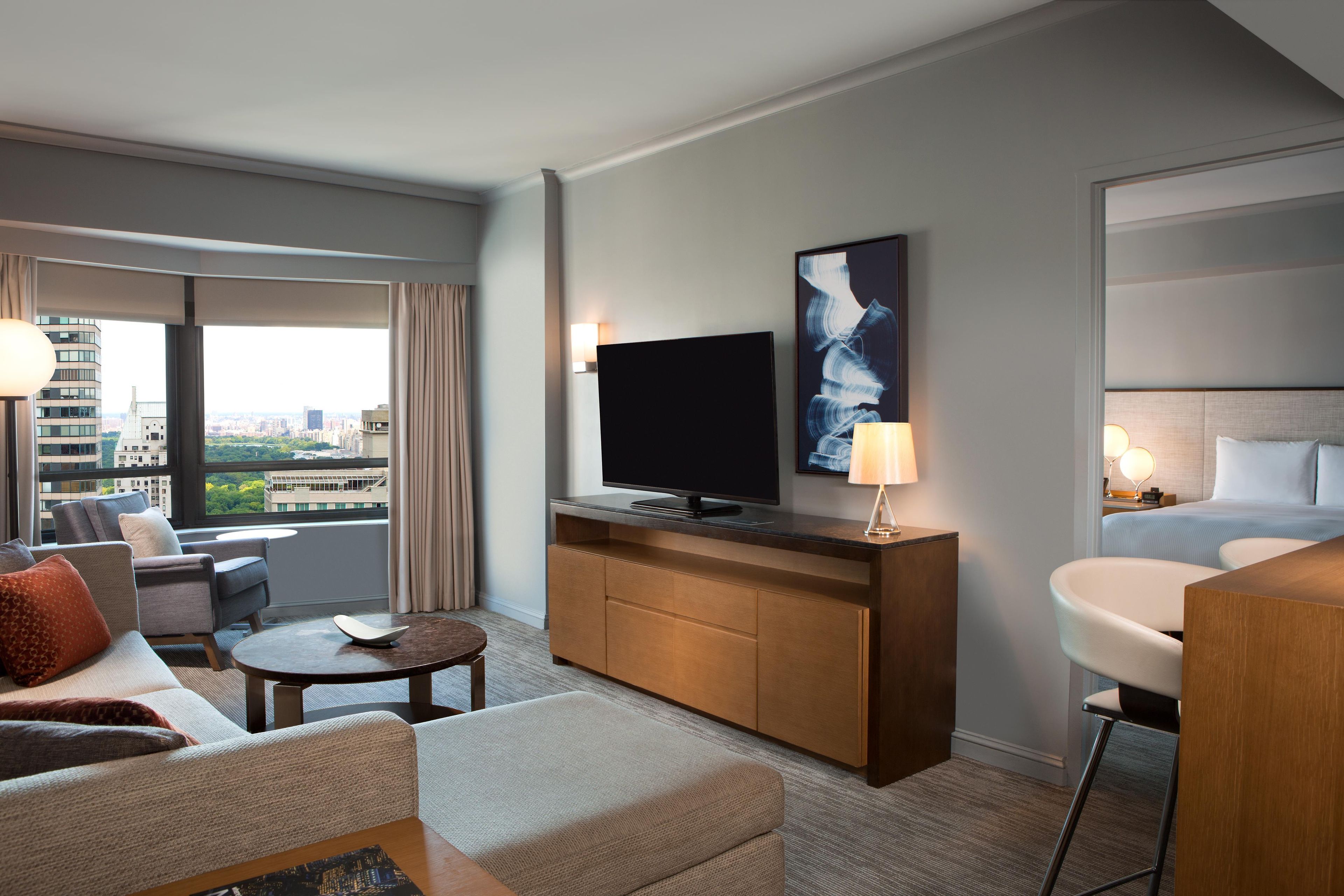 Une chambre d’hôtel dotée d’une grande fenêtre, d’un téléviseur à écran plat, d’un lit, d’un coin salon avec une table basse et offrant une vue sur le paysage urbain.