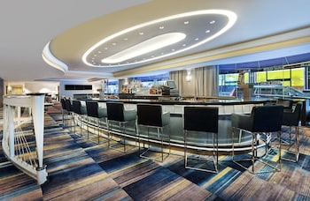 A modern dining area with marble tables, wooden chairs, and a central island with a decorative vase. at New York Hilton Midtown
