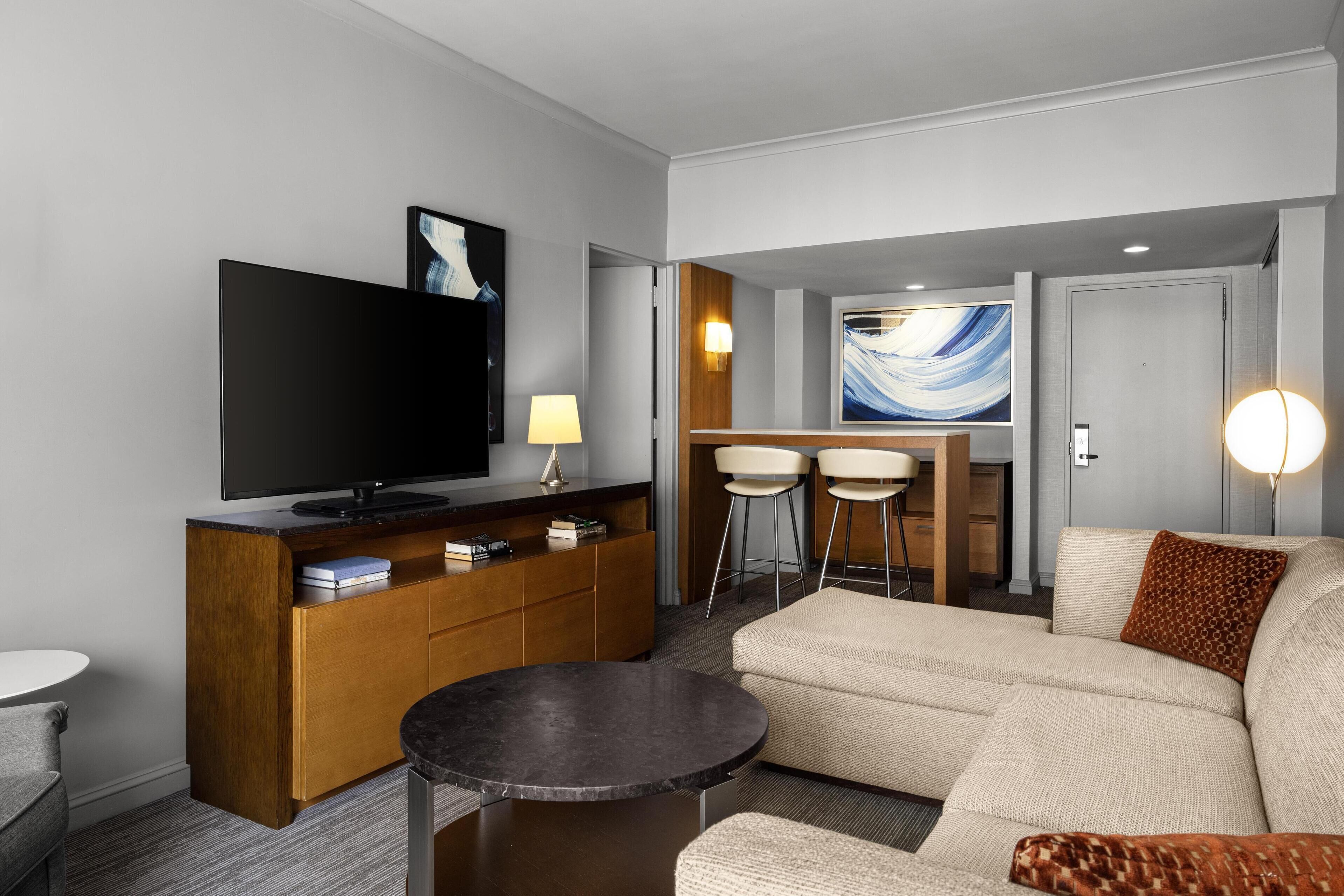 Una habitación de hotel moderna con una televisión de pantalla plana, una consola de madera, un sofá y un comedor con dos sillas y una mesa.