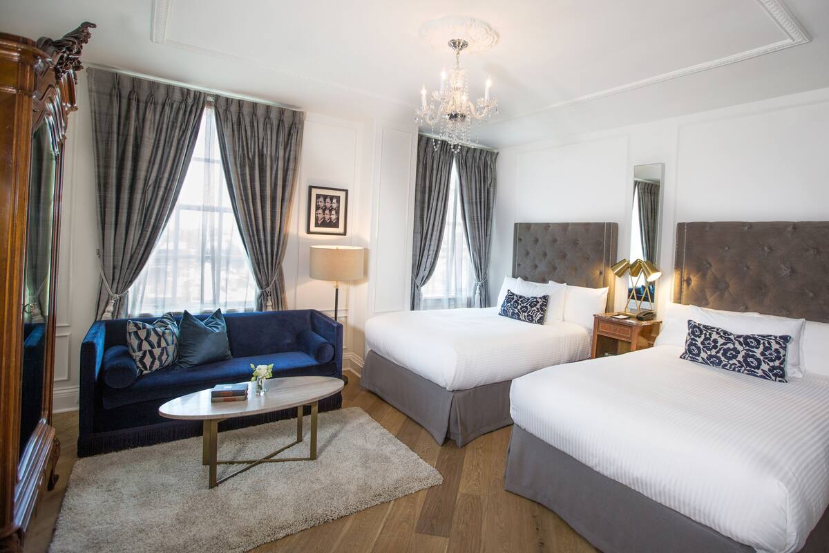 A hotel room with two beds, a sofa, a chandelier, and a large mirror.
