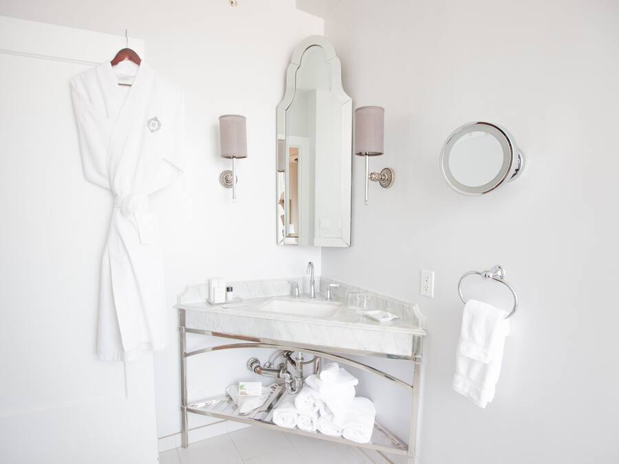 A modern bathroom with a glass vanity, a large mirror, a towel rack, and a robe hanging on a door.