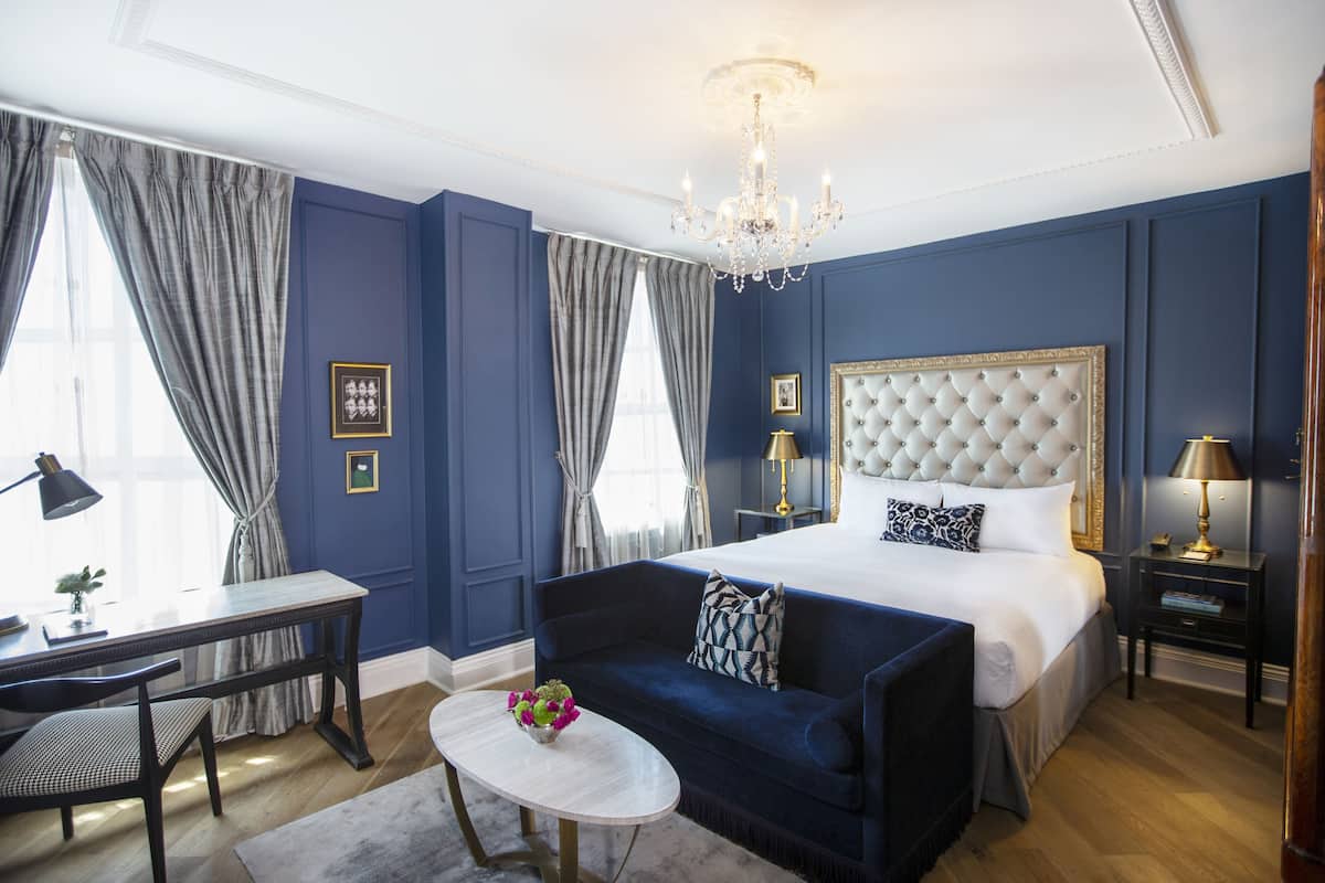A bedroom with a large bed, a sofa, a desk, and a chandelier.