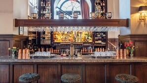 A bar with a wooden counter, multiple stools, and a variety of bottles and glasses. - The Culver Hotel (Culver City)
