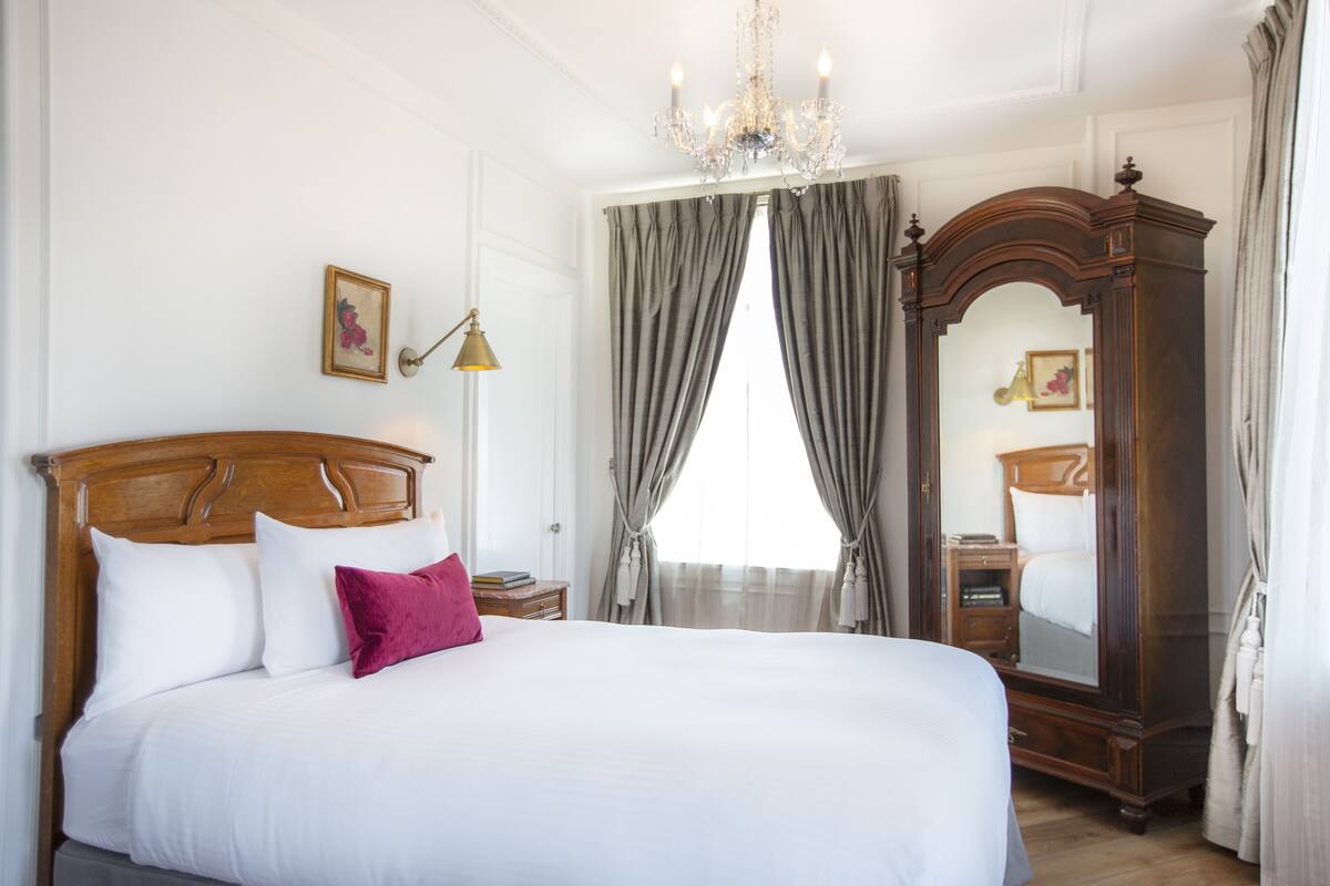 A neatly arranged bedroom with a large bed, a wooden headboard, a chandelier, and a mirror.
