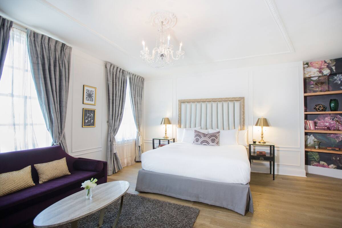 A well-lit bedroom with a large bed, a sofa, a coffee table, and a chandelier.