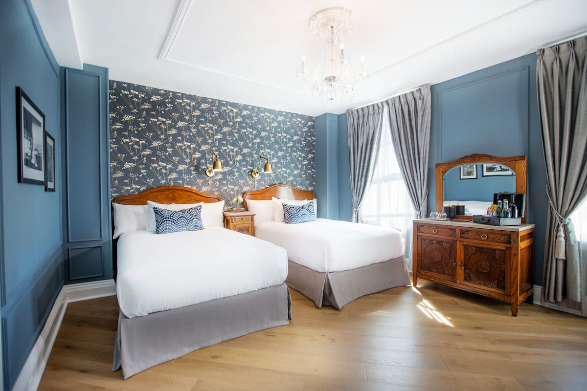 A hotel room with two beds, a wooden dresser, and a chandelier.