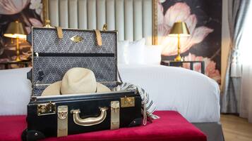 A bed with a red upholstered headboard, a suitcase with a hat, and two bedside lamps.