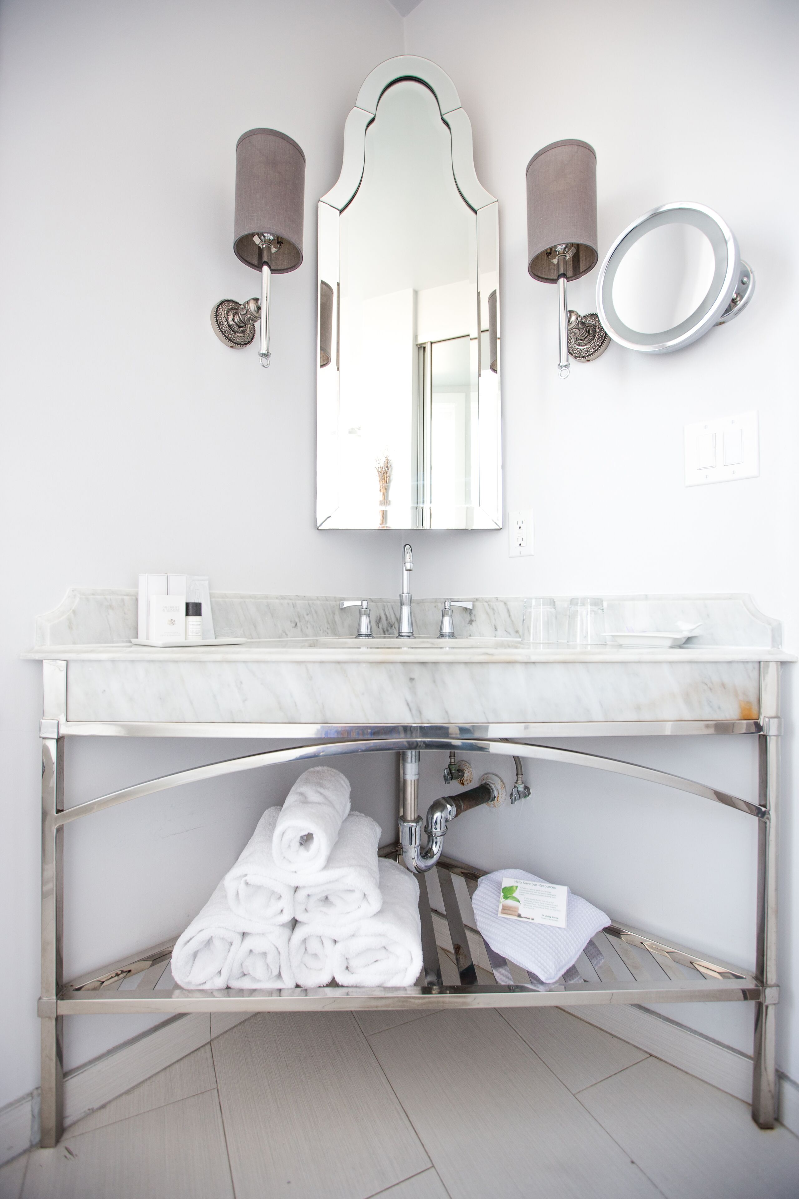 A modern bathroom with a marble sink, a large mirror, and two wall-mounted sconces.