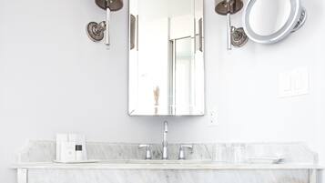 A modern bathroom with a marble sink, a large mirror, and two wall-mounted sconces.