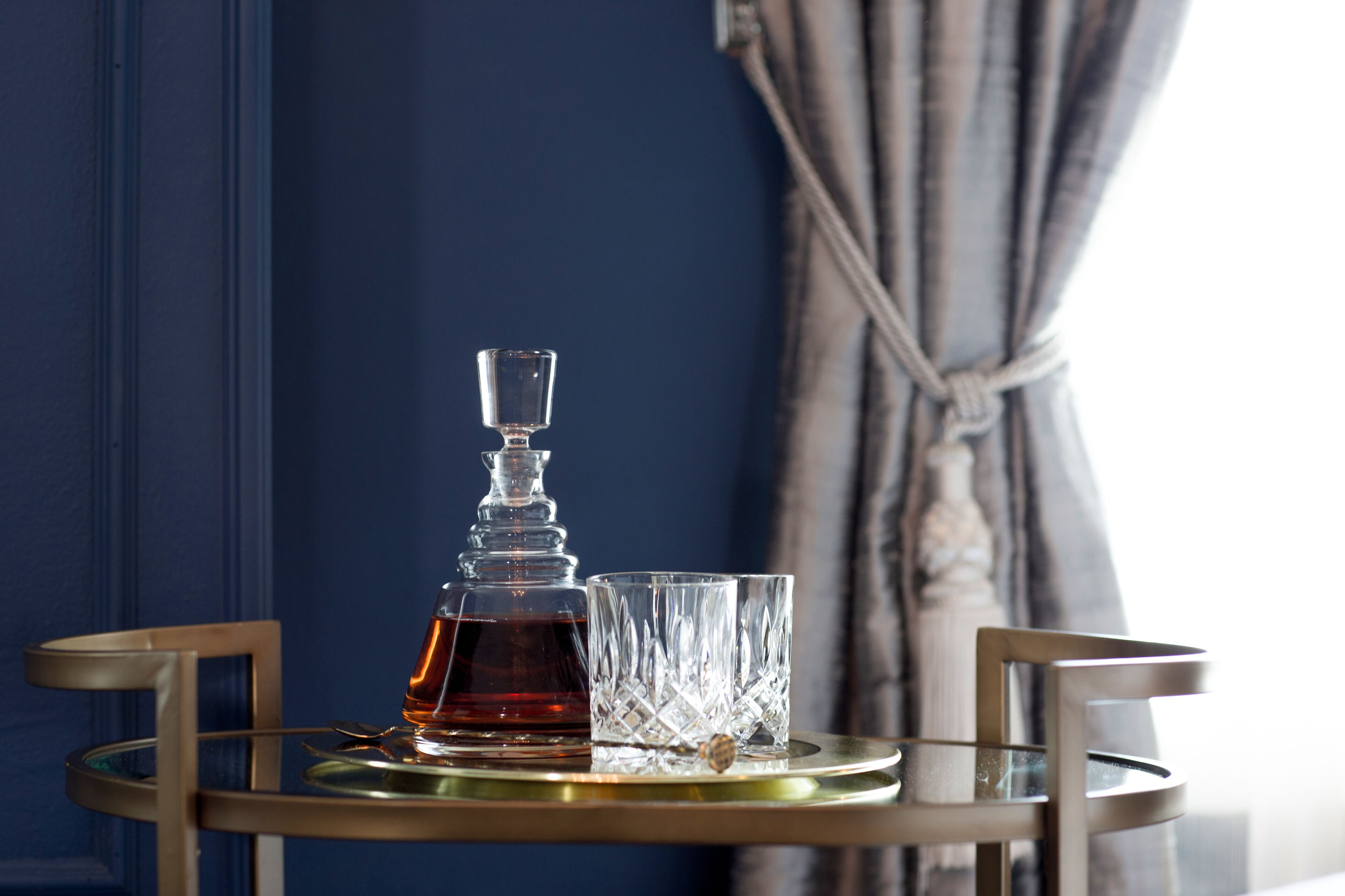 A glass decanter and two glasses on a round table with a gold tray.
