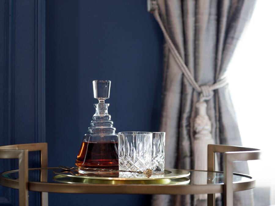 A glass decanter and two glasses on a round table with a gold tray.