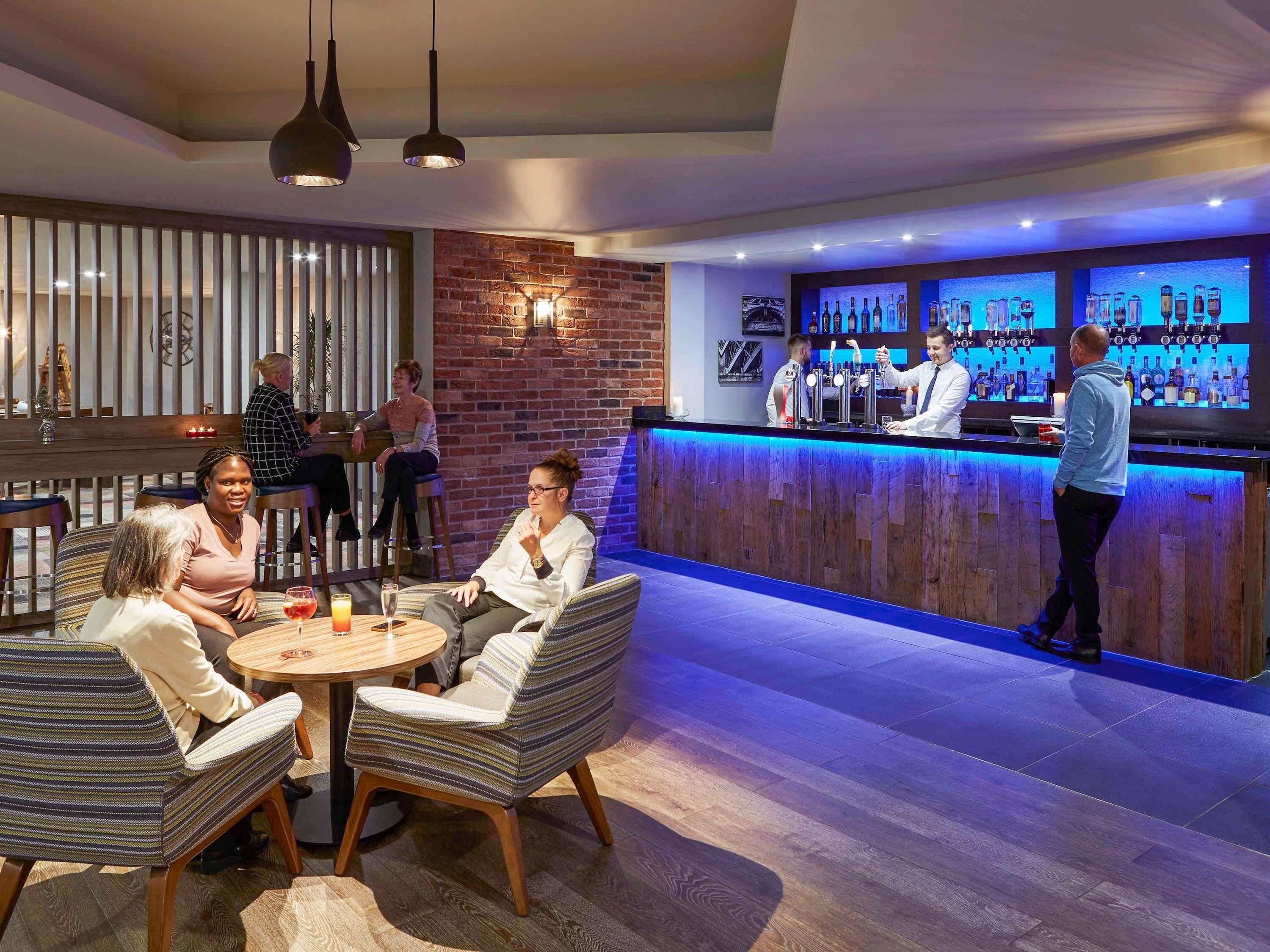 Een bar met een toonbank, barstoelen en een zithoek met ronde tafels en gestreepte stoelen.