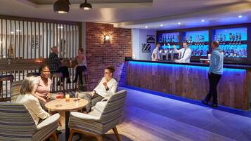 Een bar met een toonbank, barstoelen en een zithoek met ronde tafels en gestreepte stoelen.