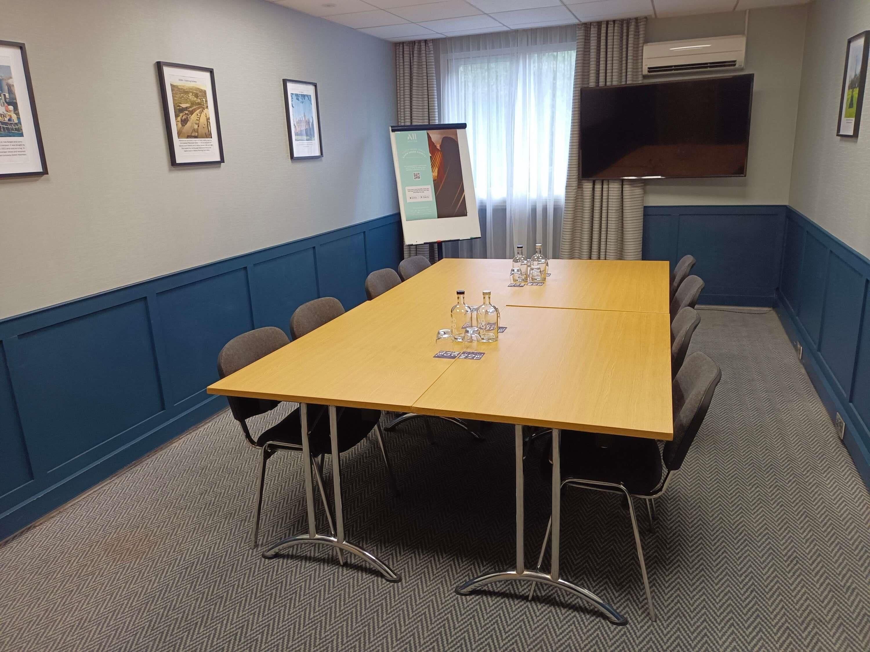 A conference room with a long table, chairs, framed pictures on the wall, and a mounted TV.
