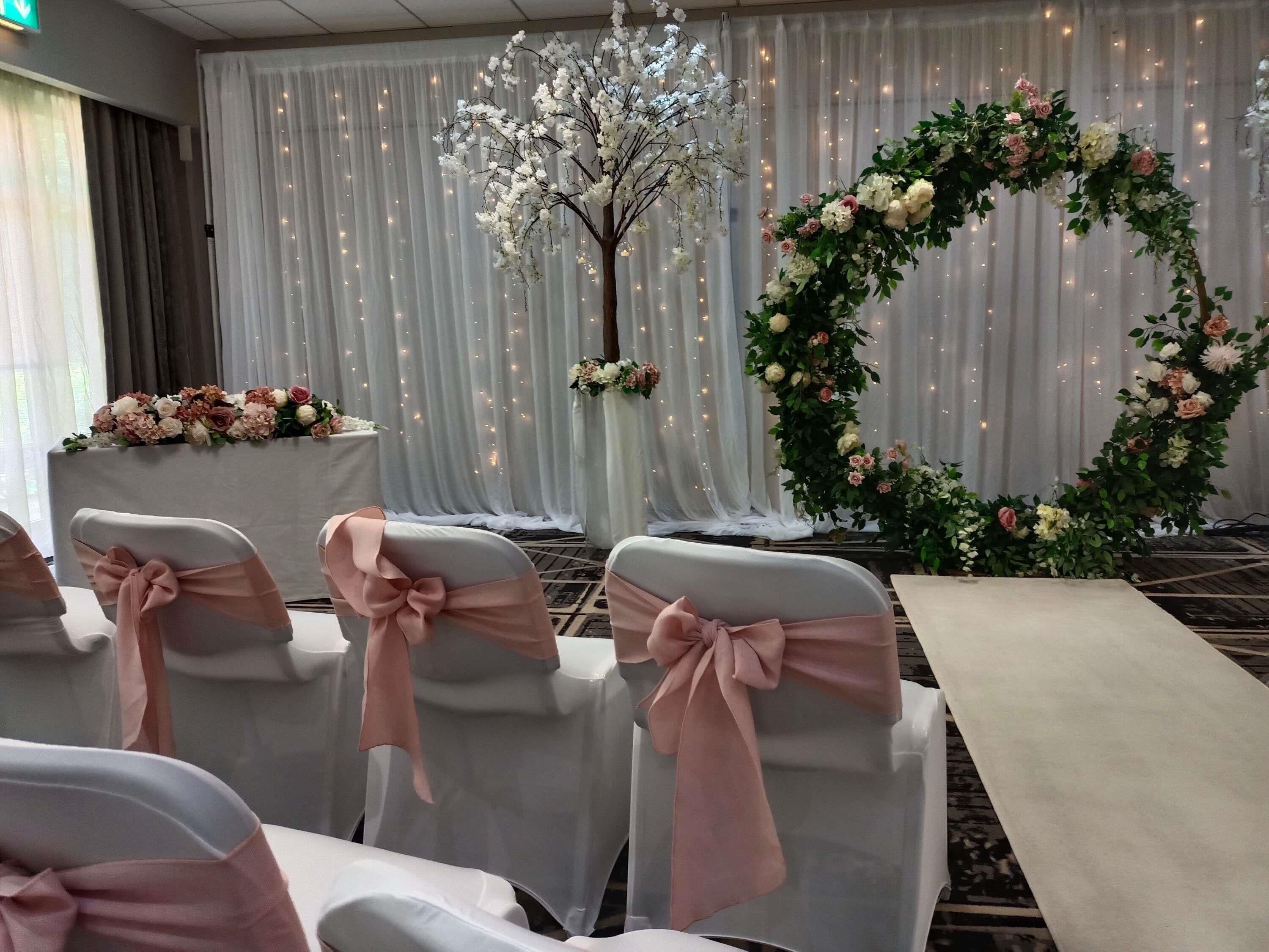 A room with rows of chairs with pink sashes, a floral arrangement, and a large circular floral wreath.