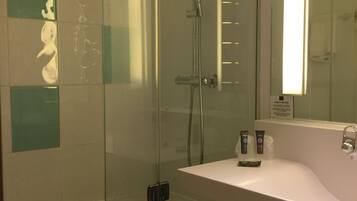 A modern bathroom with a glass-enclosed shower, a white sink, and a safety notice on the wall.
