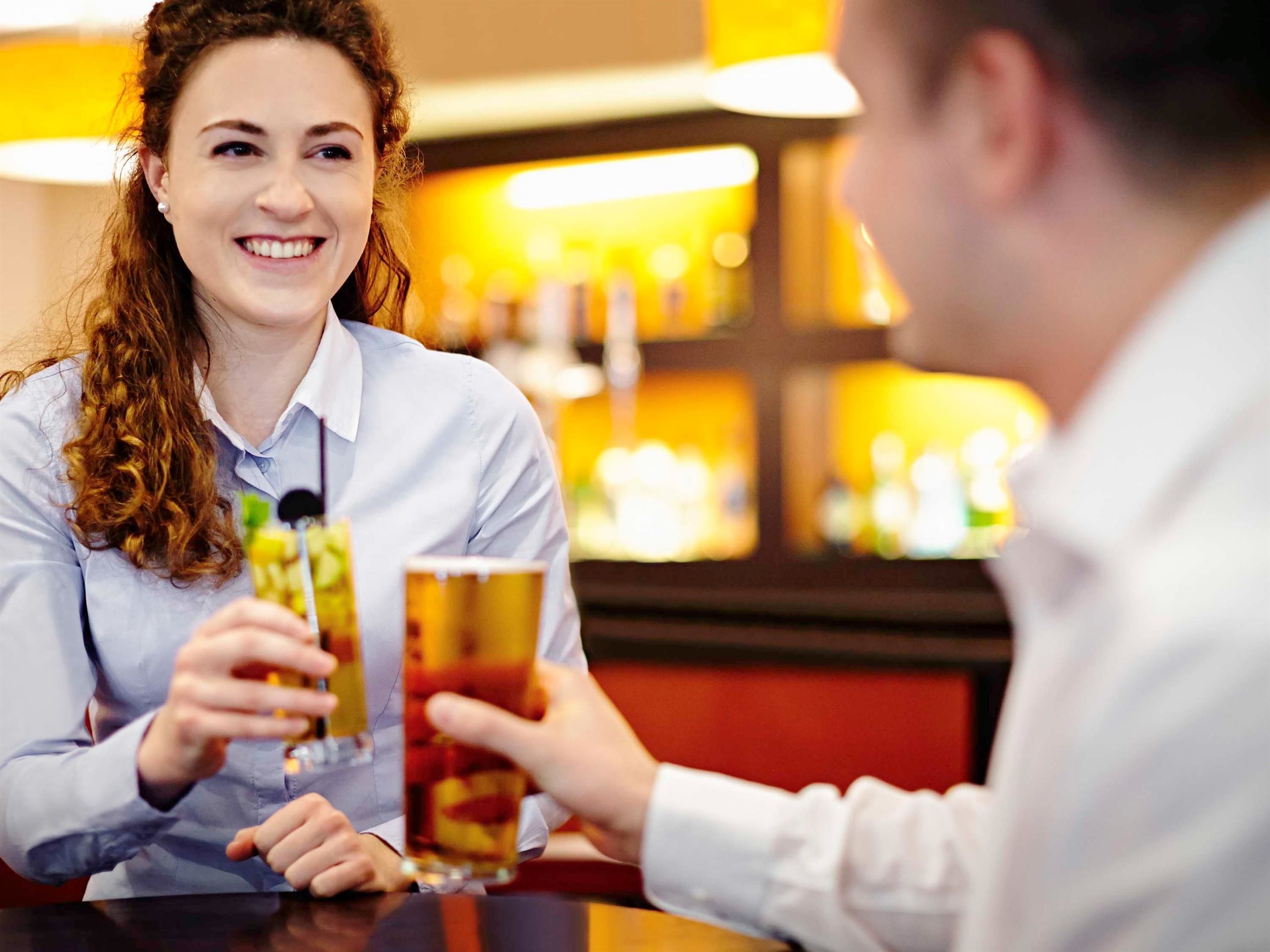 Une personne tenant un verre contenant une boisson de couleur ambrée dans un bar, avec un arrière-plan flou.