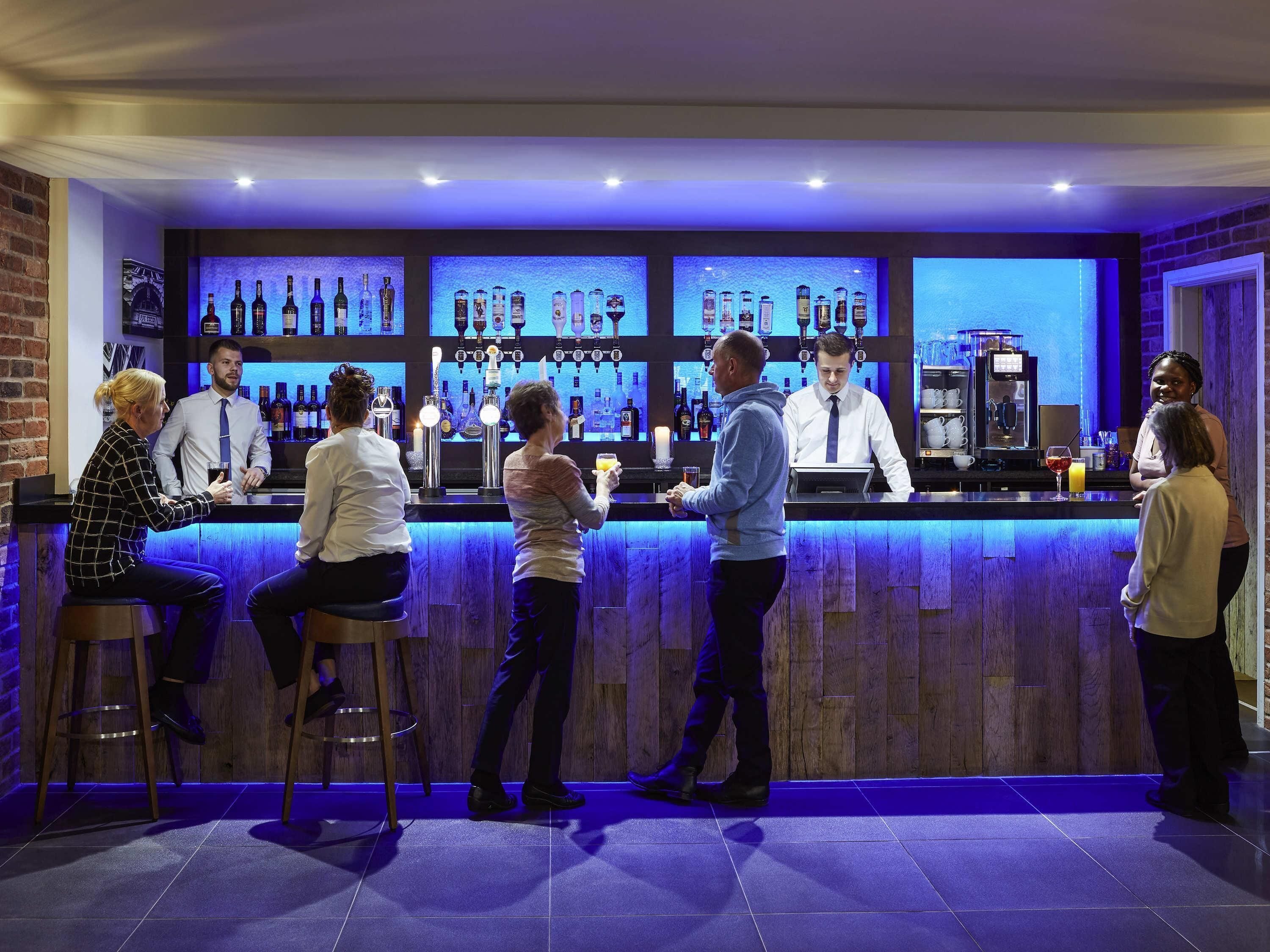 Uma área de bar com banquetas, balcão e uma seleção de garrafas.