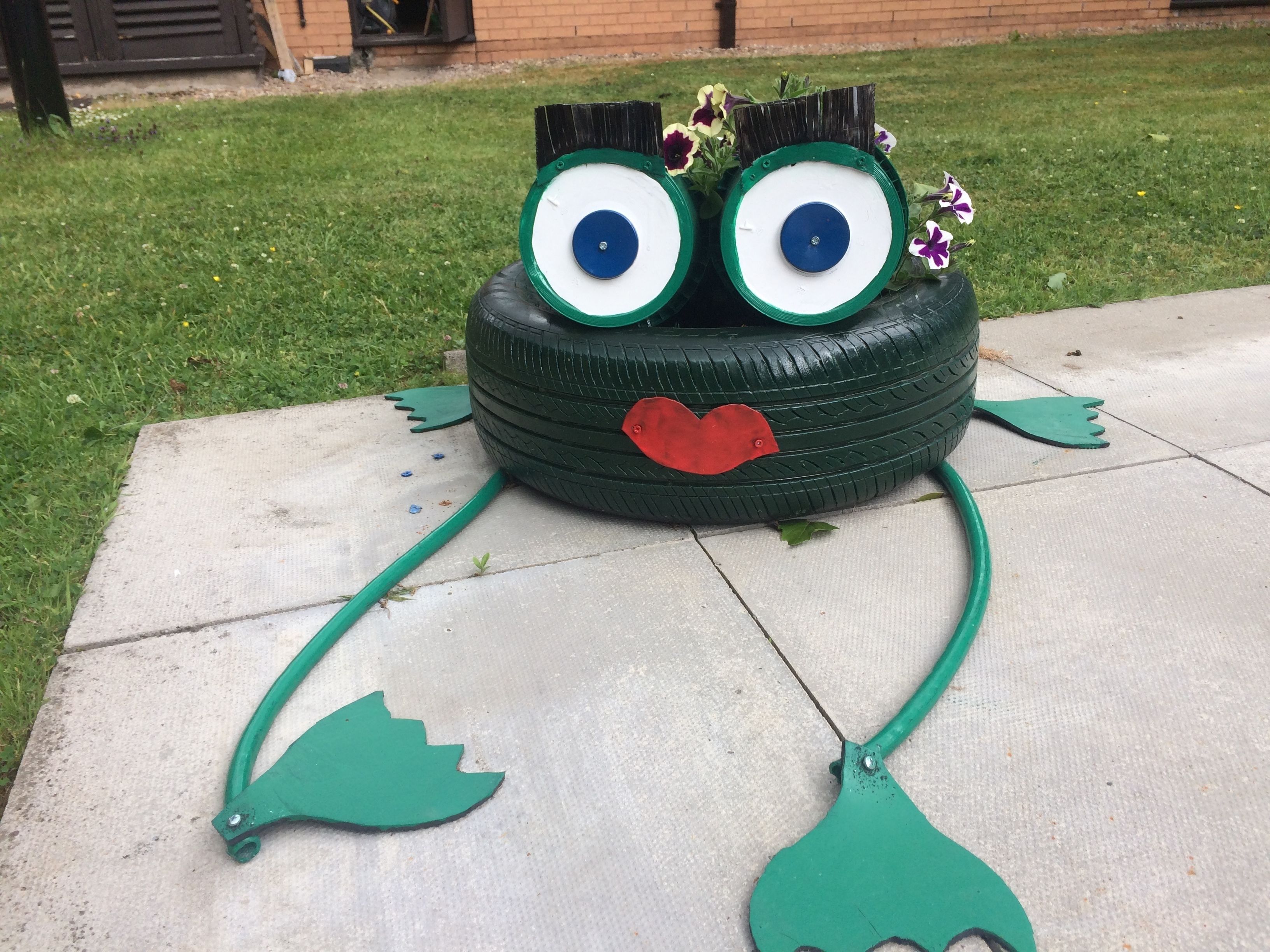 A tire transformed into a whimsical character with large eyes, a red mouth, and green limbs.