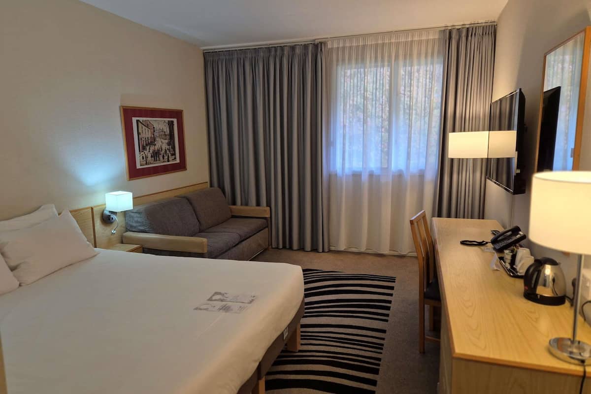 Ein Hotelzimmer mit einem Bett, einem Sofa, einem Schreibtisch mit Telefon und einem Fernseher.