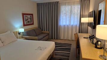 A hotel room with a bed, a sofa, a desk with a telephone, and a television.