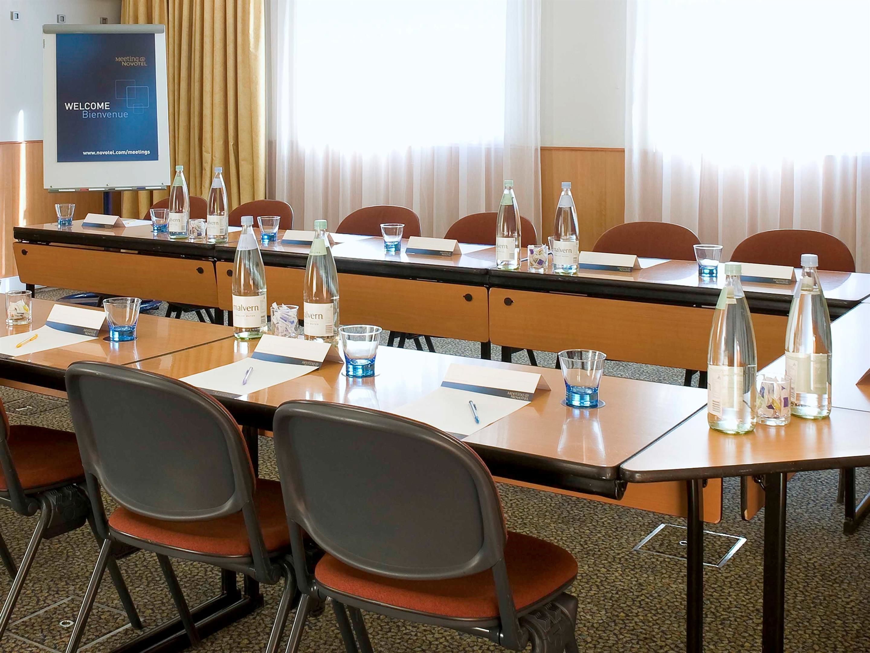 A conference room with a long table, chairs, water bottles, and a presentation screen.