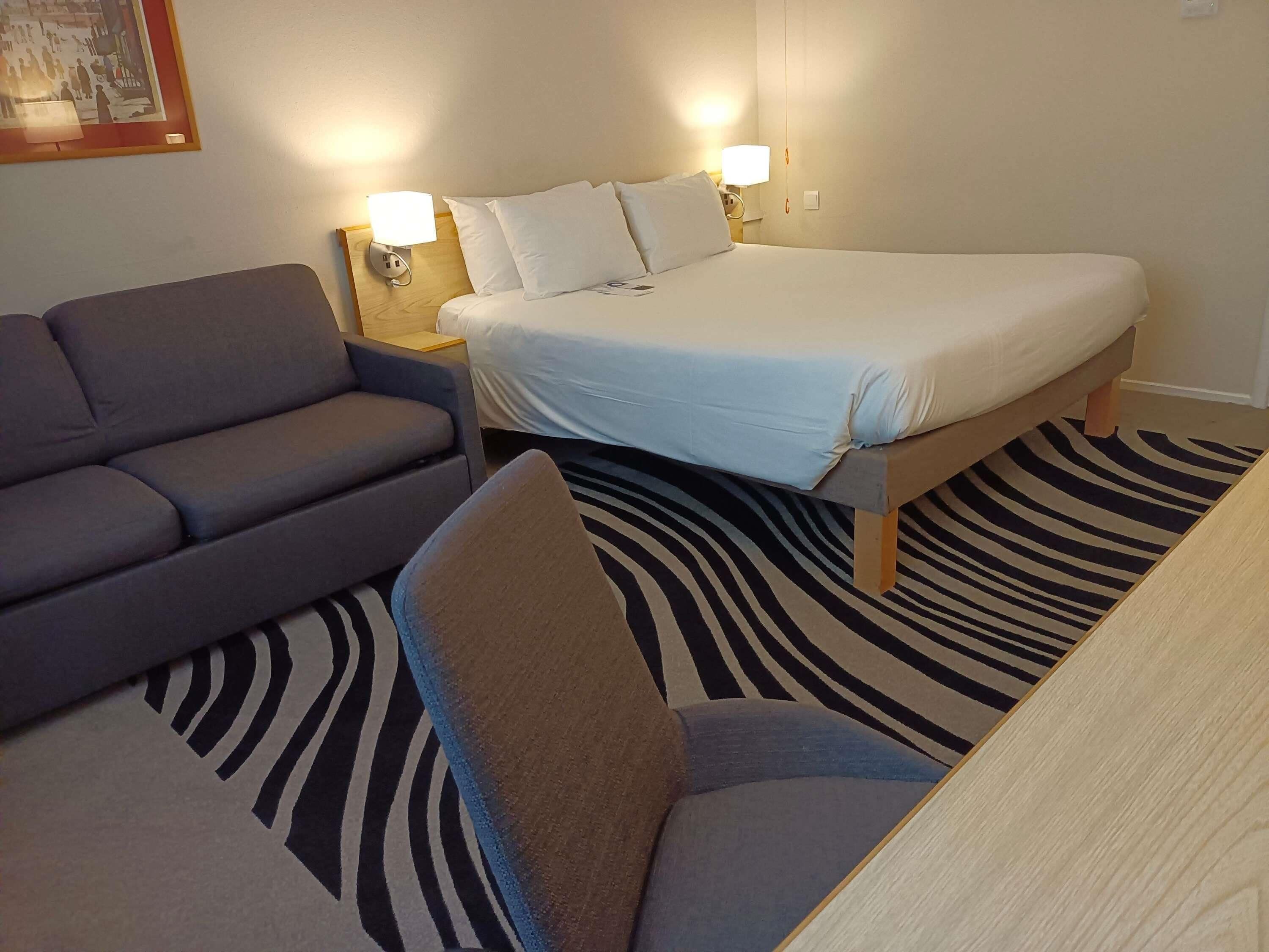 Et hotelværelse med en seng, en sofa, et natbord og en måtte med zebramønster.