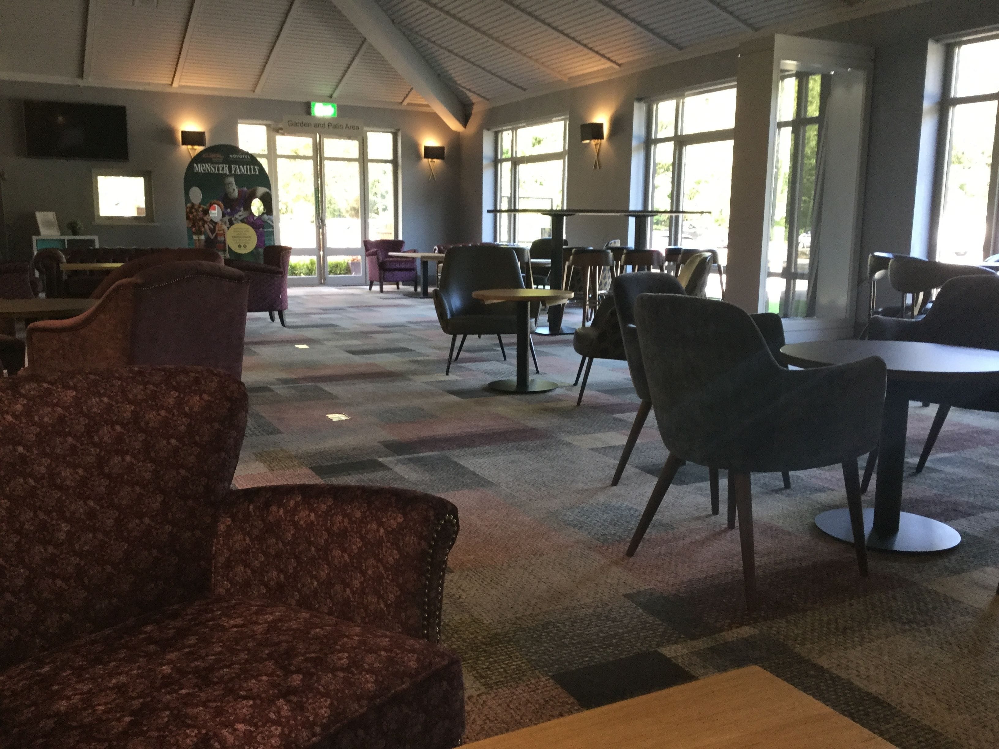 A spacious indoor area with multiple seating arrangements, including chairs and tables, and a large window providing natural light.