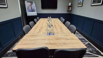 A conference room with a long table, chairs, a projector screen, and framed pictures on the walls.
