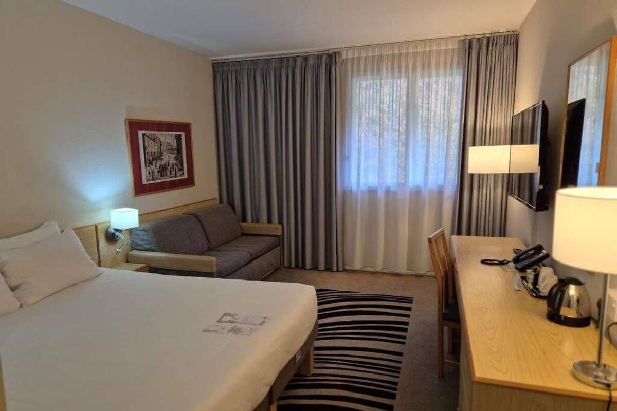 Habitación de hotel con dos camas, un escritorio, una silla, un televisor y una ventana con cortinas.