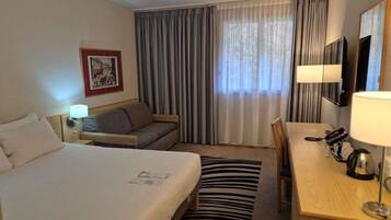 A hotel room with two beds, a desk, a chair, a television, and a window with curtains.