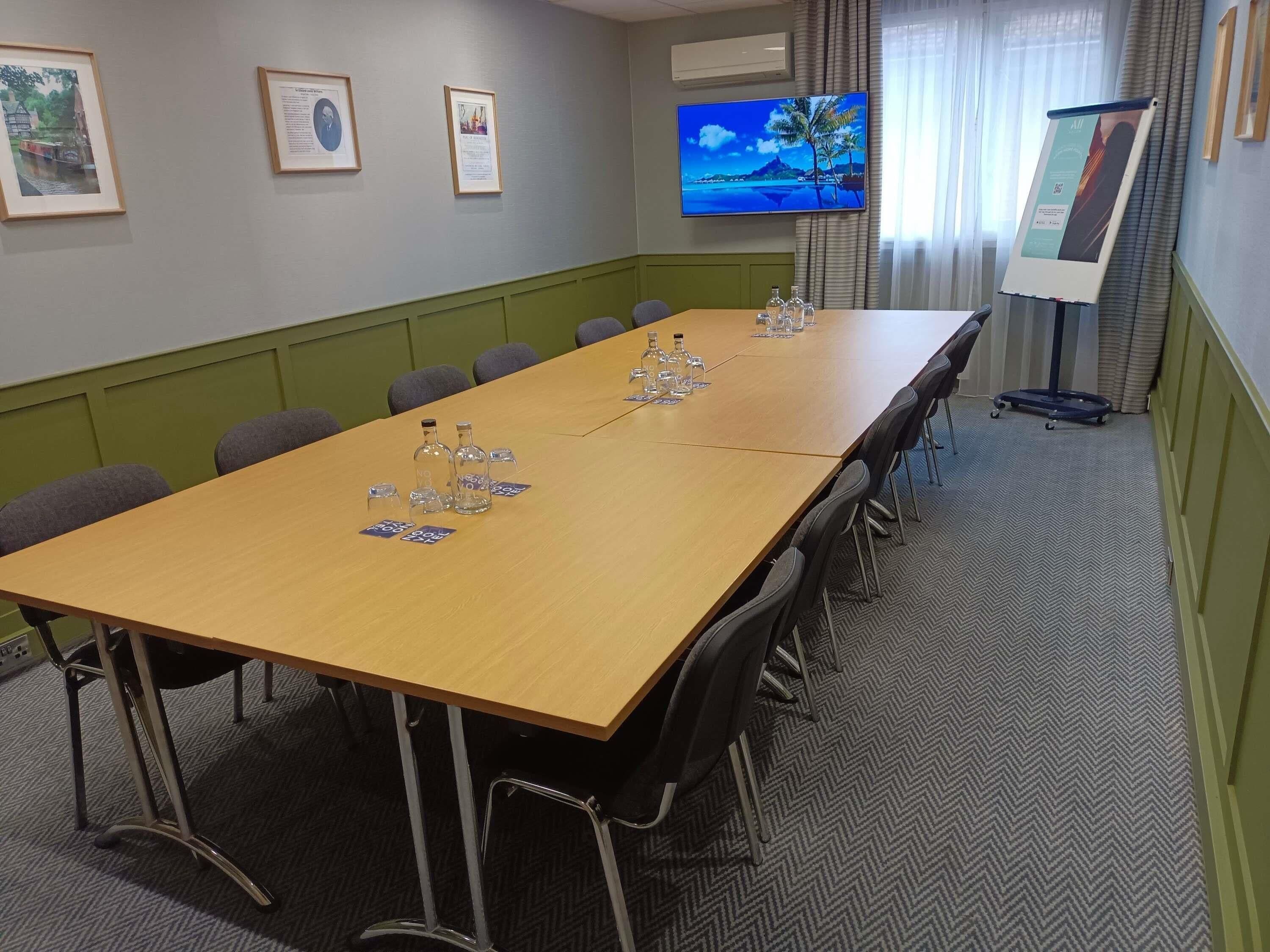A conference room with a long table, chairs, a TV, framed certificates, and a projector screen.