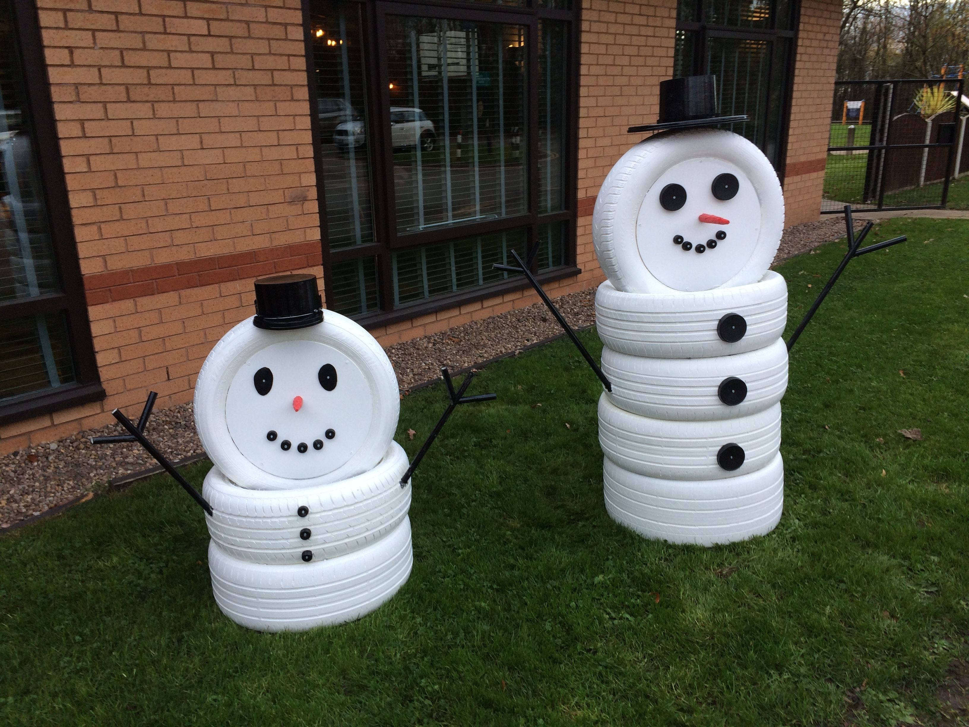 Two snowmen made from tires in front of a building with windows and a brick wall.